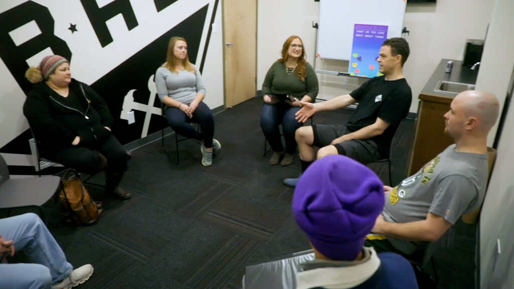 A group of adults sitting on chairs in a circle engaged in discussion.