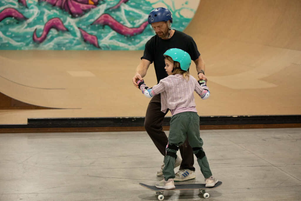 Coach Eric helps a young student on a skateboard