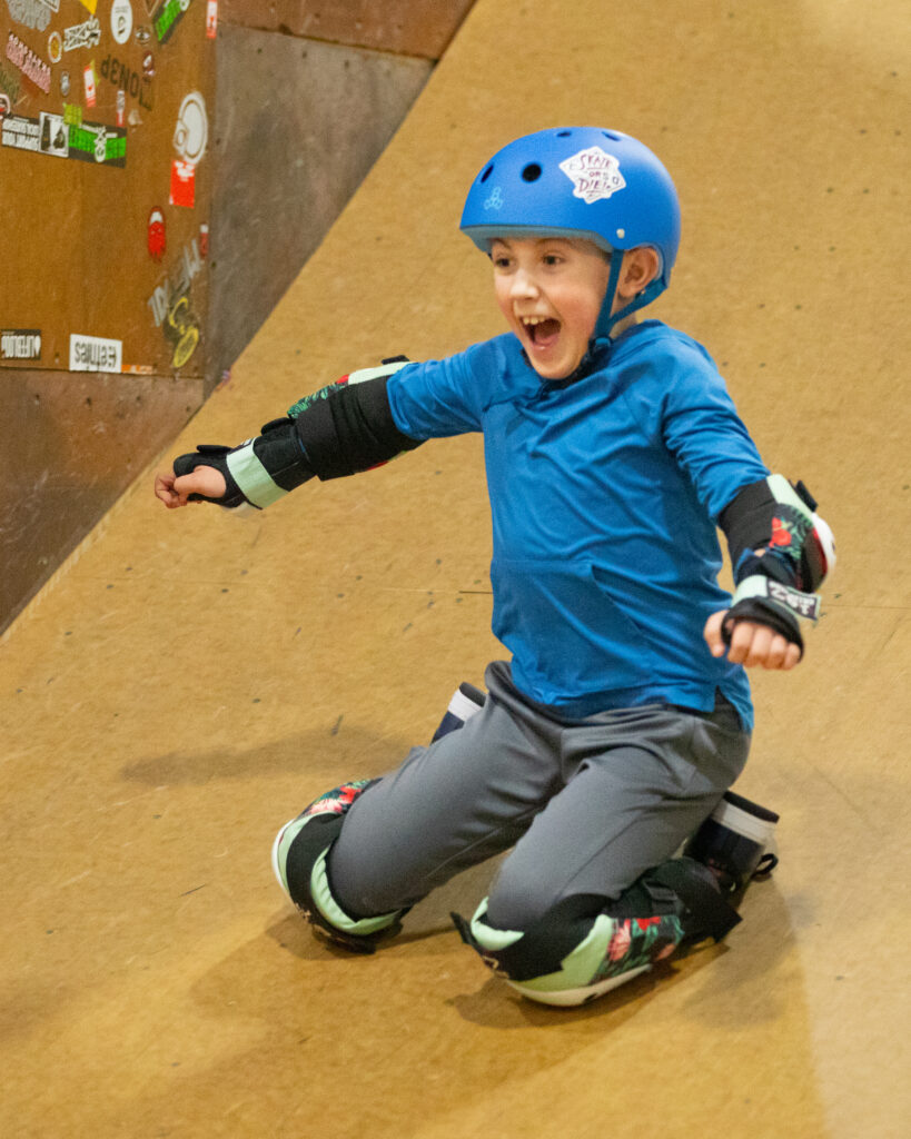 A young rider sliding down a skate ramp on his knees