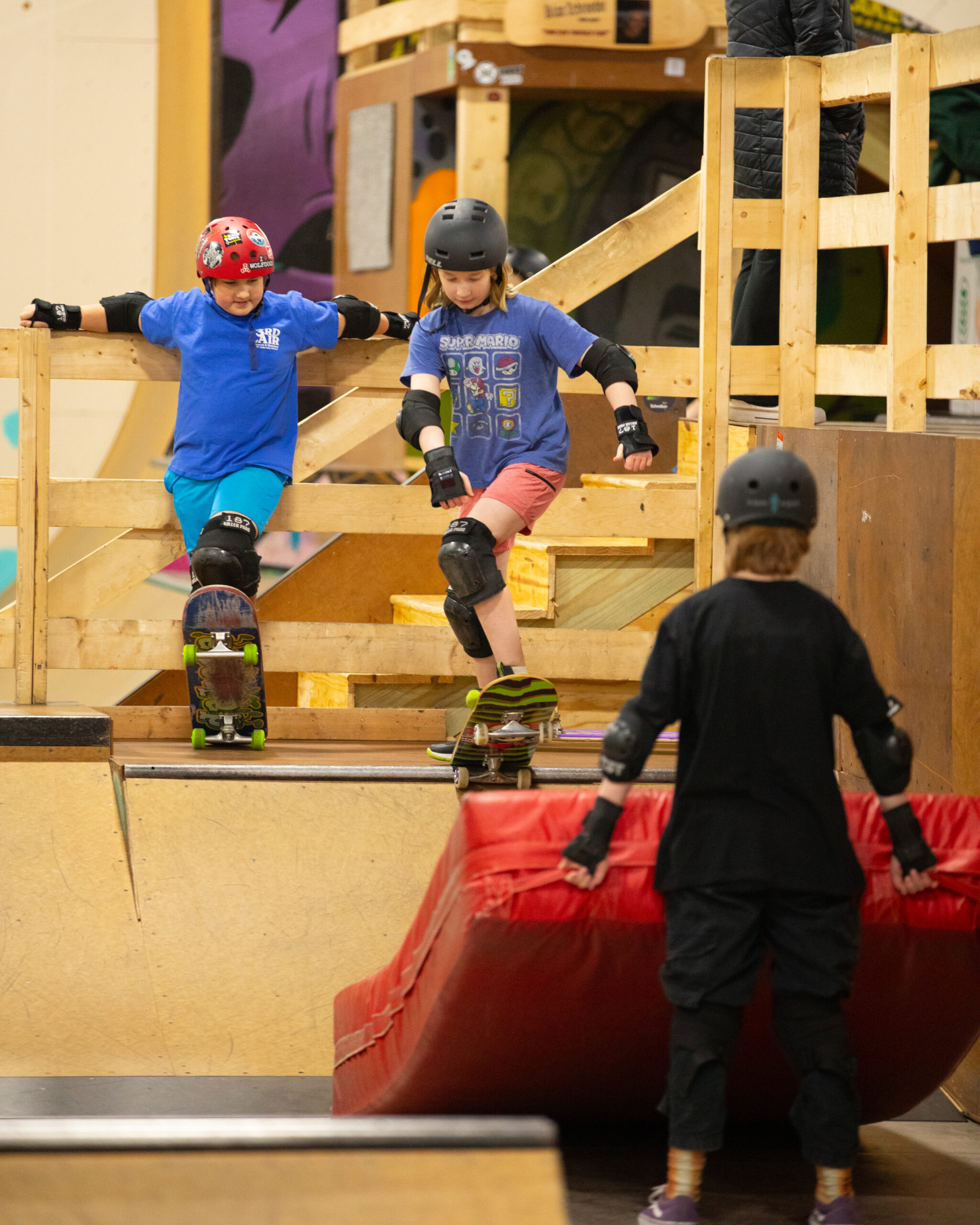 a young skateboarder holds a crash pad for a friend who is about to drop in on a skate ramp