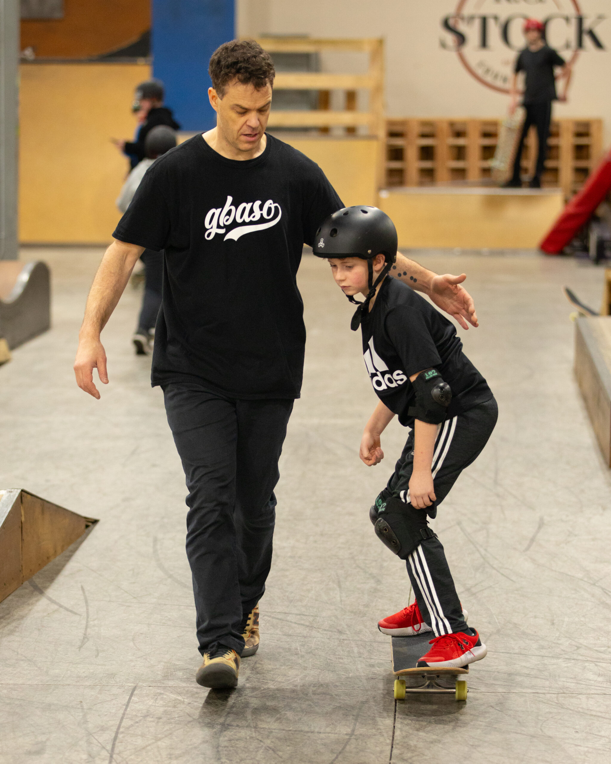 a skateboard coach walks alongside a young skateboard student