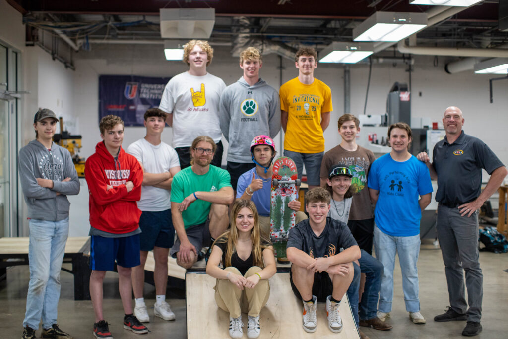 High school students pose in front of a skateboard ramp that they designed and built