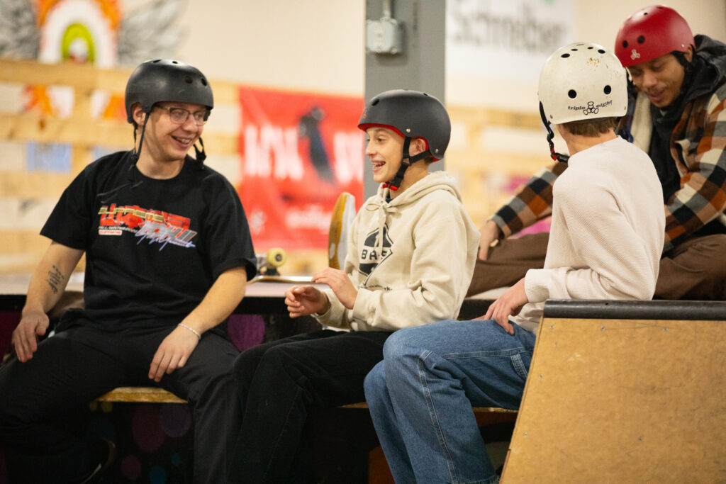 skateboarders interact and laugh while seated at GBASO skatepark