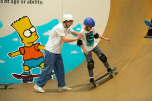 Skate coach Ryan teaches a young rider how to pump on the vert ramp