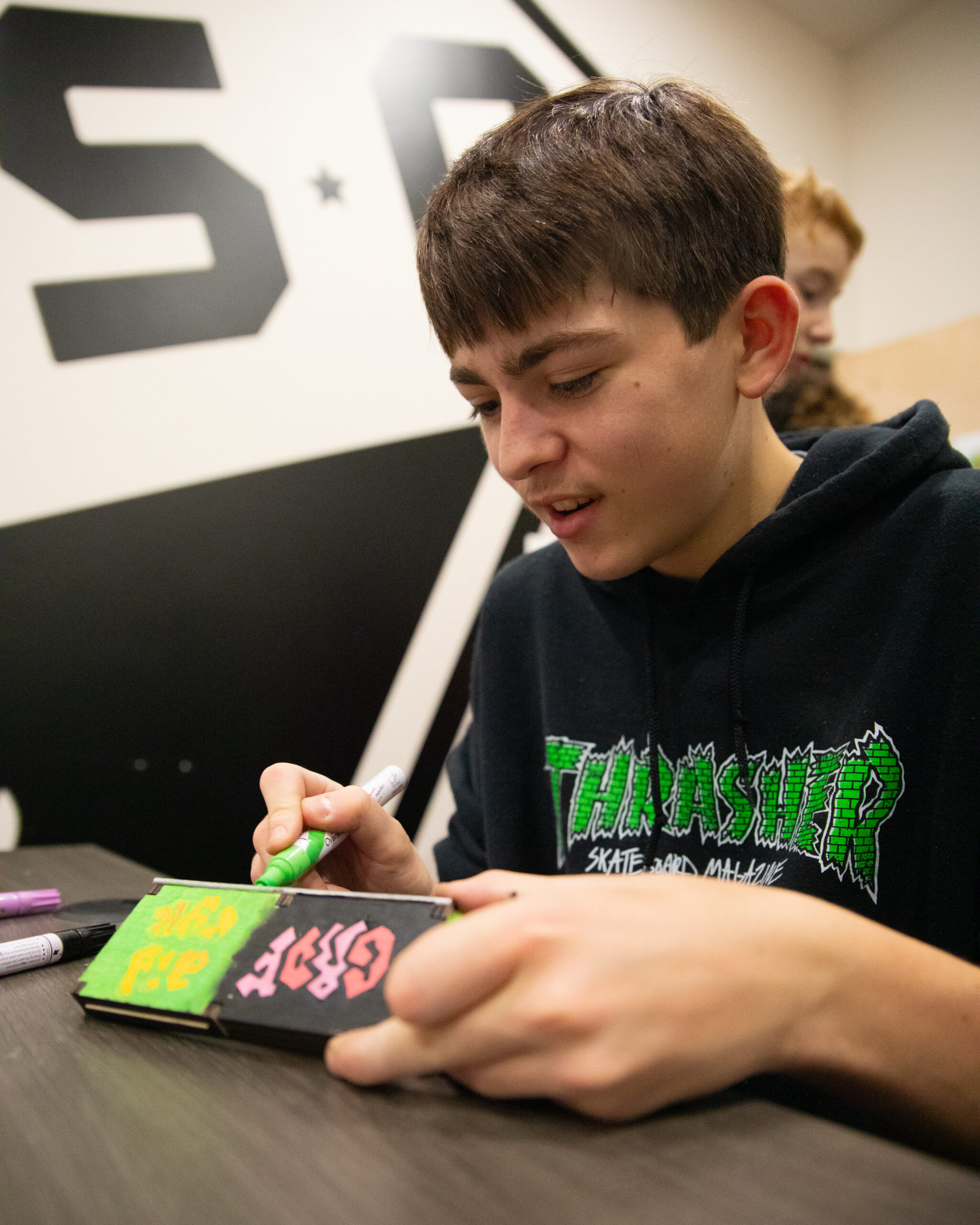 A teenage artist uses a paint pen to decorate his fingerboard park