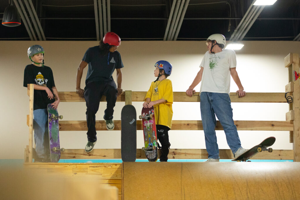 A group of skateboarders hang out and talk on top of a skate ramp