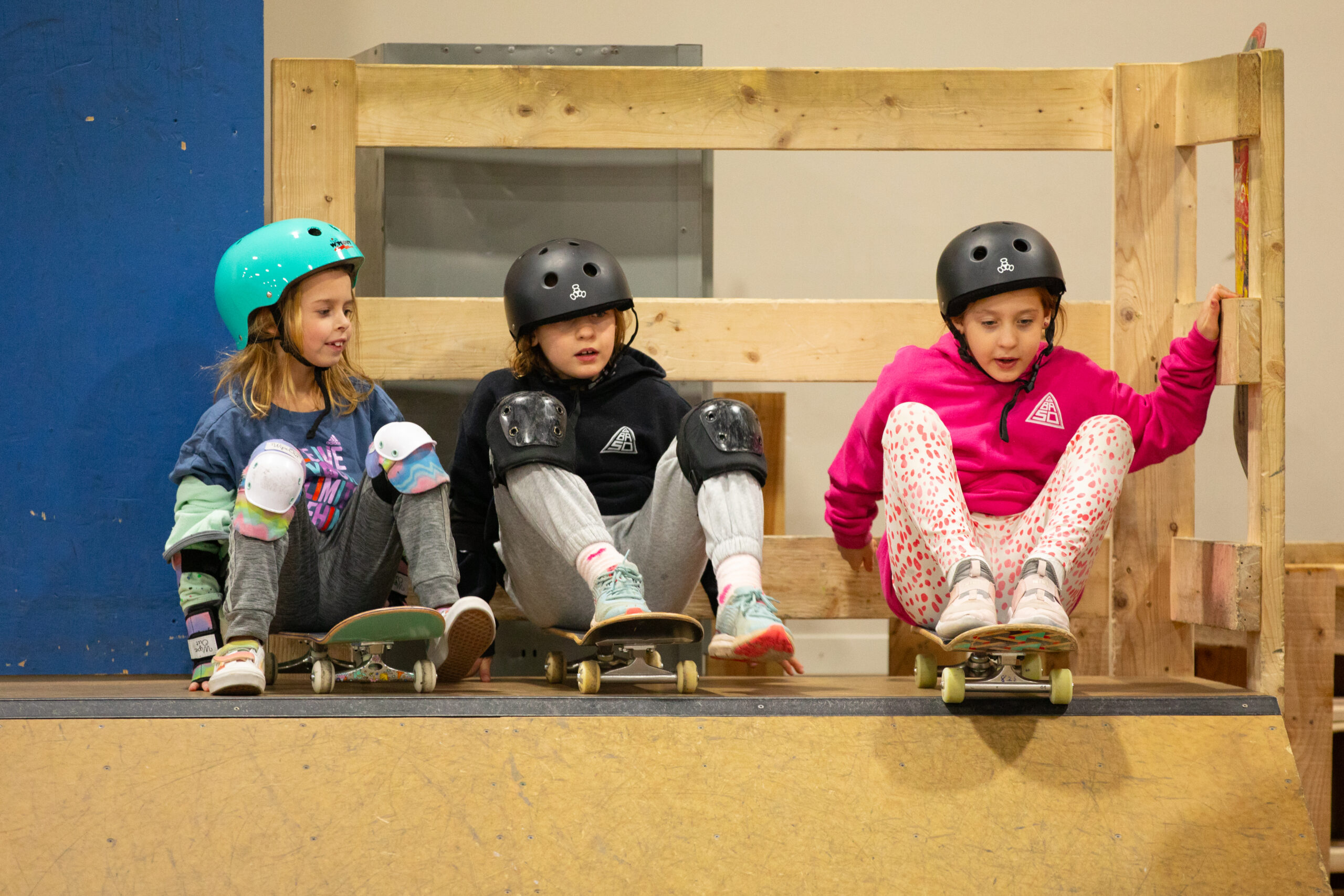 3 girls sitting on their skateboards on top of a ramp