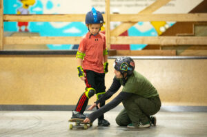A skate coach helps a young rider with his foot placement on his skateboard.